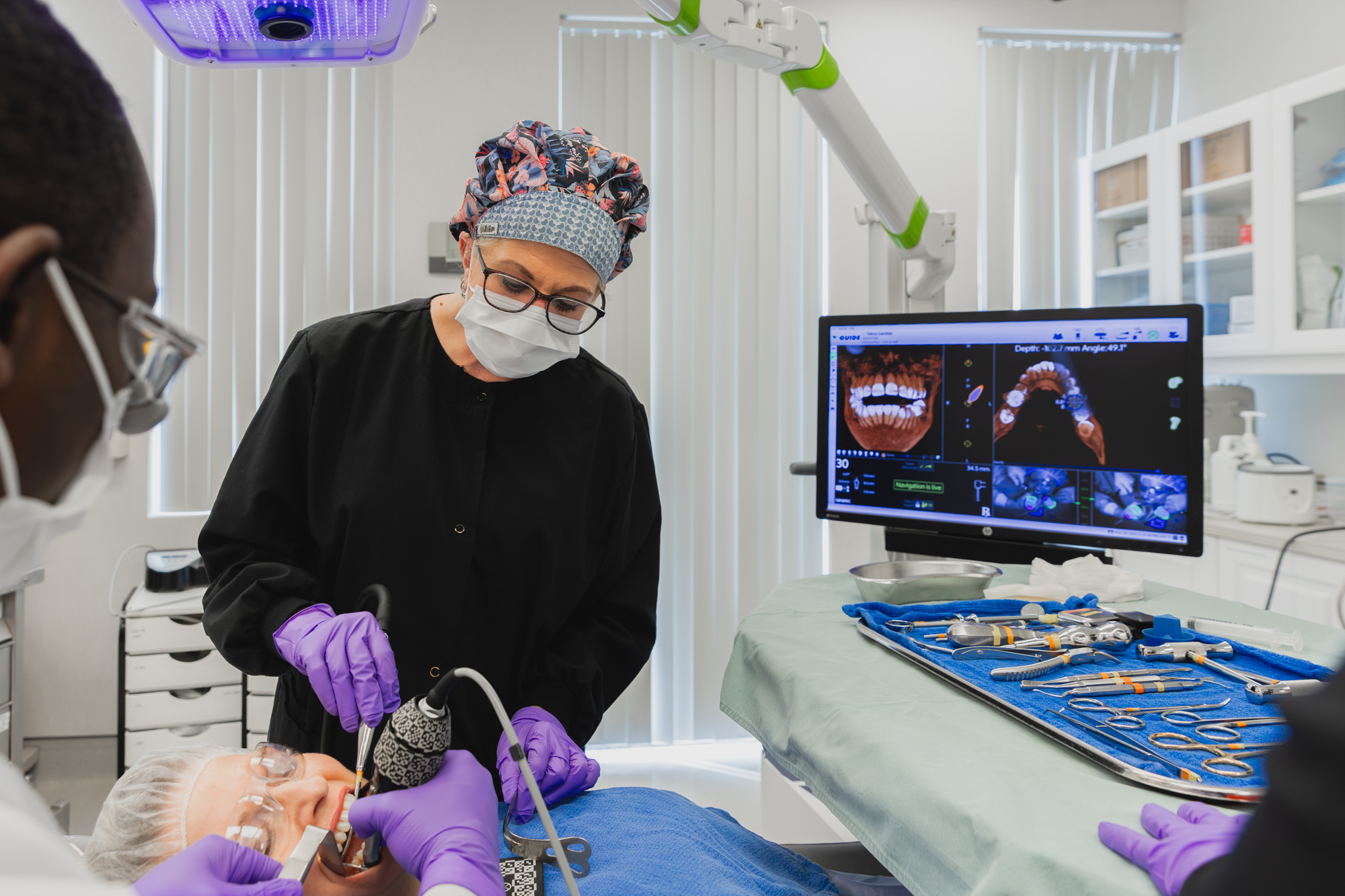  Providers at the Krupp Center perform comprehensive dental services in Towson. The providers can be seen working on the patient's mouth, a computer monitor displaying X-rays to the side, with additional dental equipment sitting on a medical tray-ready for use.